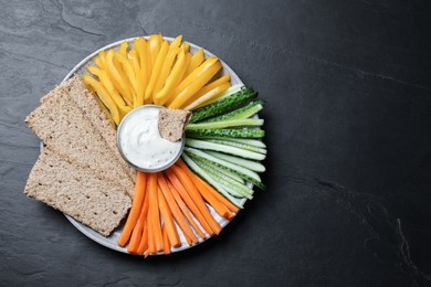 Photo of Plate with crispbreads, vegetable sticks and dip sauce on black table, top view. Space for text