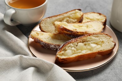 Photo of Pieces of delicious yeast dough cake and tea on light gray table, closeup