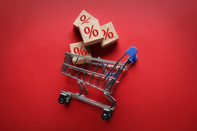 Image of Discount offer. Boxes with percent signs and shopping cart on red background, top view