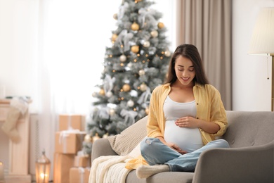 Photo of Happy pregnant woman on sofa in living room decorated for Christmas. Expecting baby