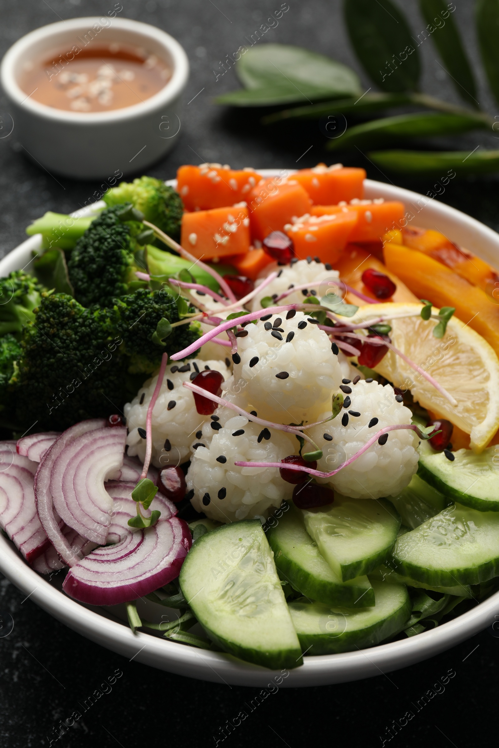 Photo of Bowl with many different vegetables and rice on grey textured table, closeup. Vegan diet