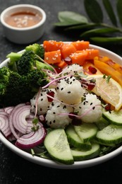 Bowl with many different vegetables and rice on grey textured table, closeup. Vegan diet