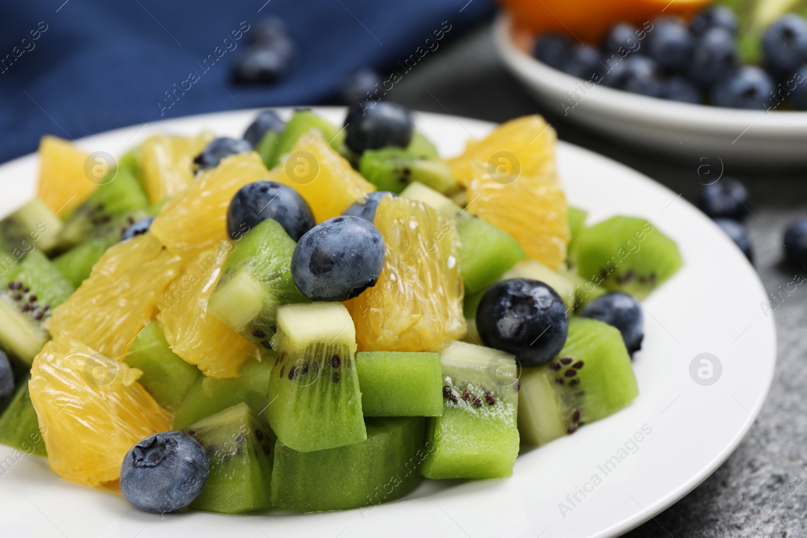 Photo of Plate of tasty fruit salad on grey textured table, closeup