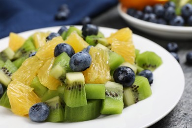 Plate of tasty fruit salad on grey textured table, closeup