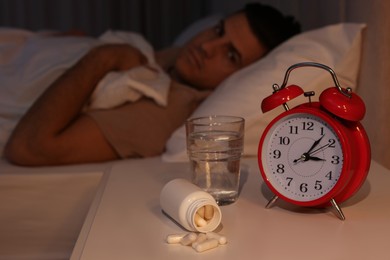 Man suffering from insomnia in bed at night, focus on pills and alarm clock