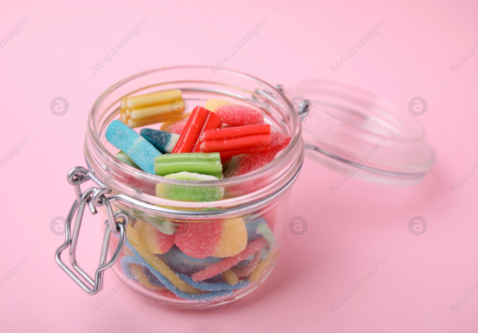 Photo of Tasty jelly candies in open jar on pink background, closeup