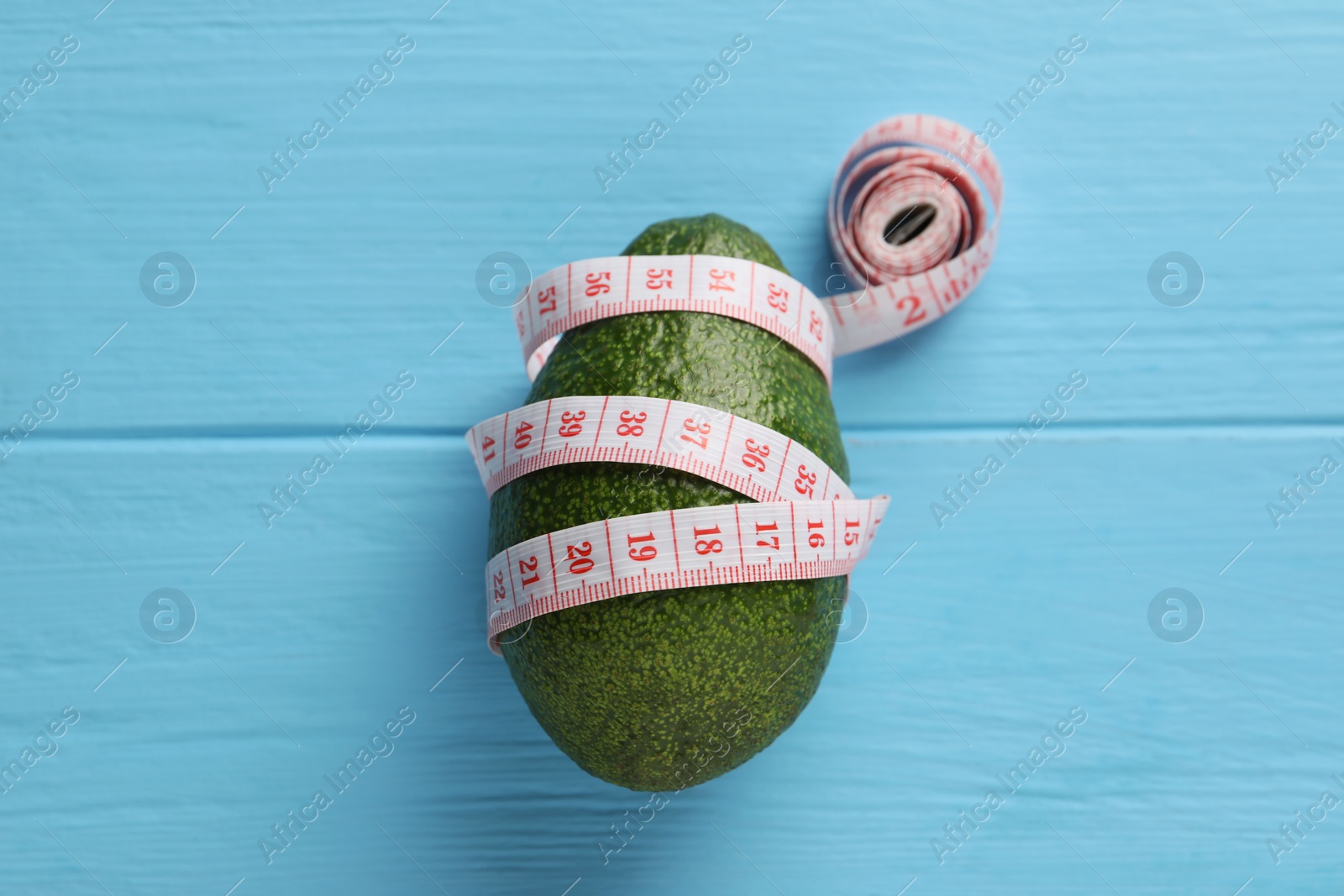 Photo of Healthy diet. Avocado and measuring tape on light blue wooden table, top view