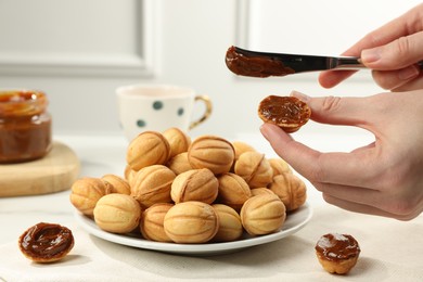 Woman spreading boiled condensed milk onto walnut shaped cookie indoors, closeup