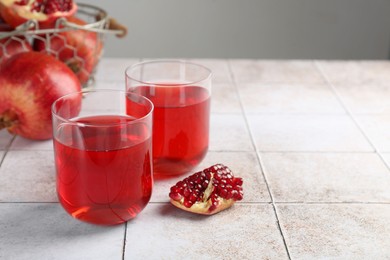 Photo of Tasty pomegranate juice in glasses and fresh fruits on white tiled table. Space for text
