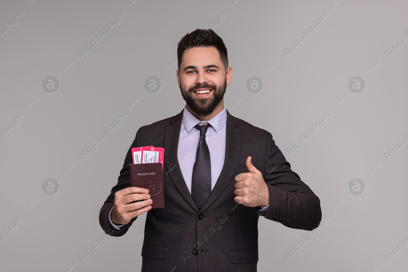 Photo of Happy businessman with passport and tickets showing thumb up on grey background