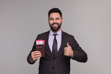 Happy businessman with passport and tickets showing thumb up on grey background