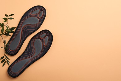 Photo of Pair of orthopedic insoles and leaves on pale orange background, top view. Space for text