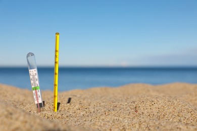 Weather thermometers in sand near sea, space for text