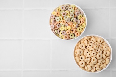 Photo of Tasty cereal rings in bowls on white tiled table, flat lay. Space for text