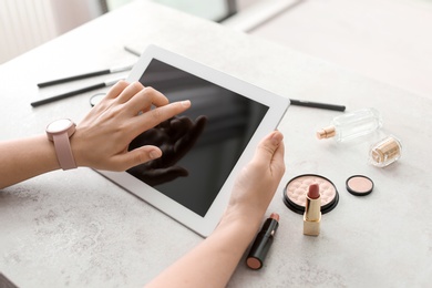 Young woman with makeup products using tablet at table. Beauty blogger