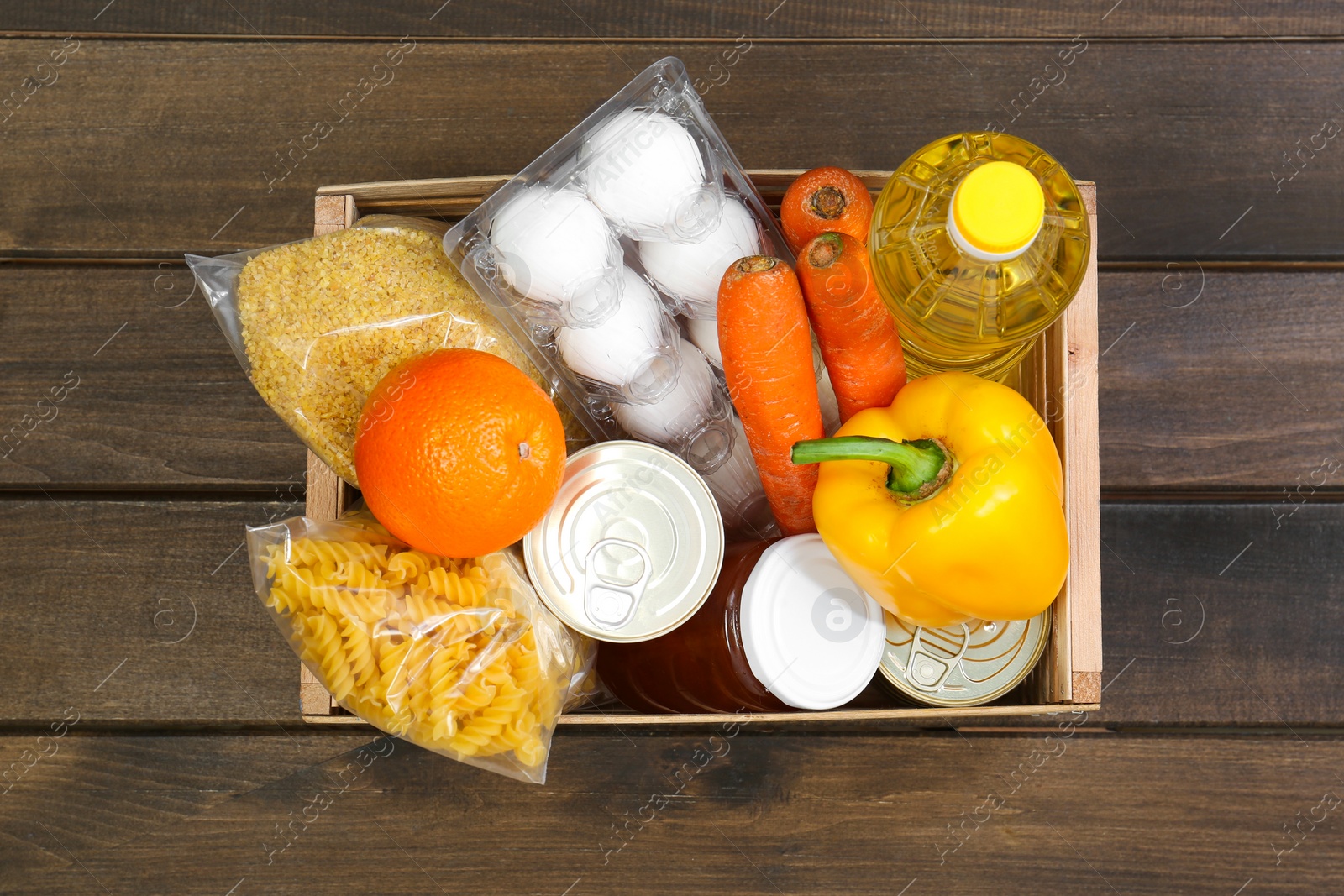 Photo of Crate with donation food on wooden table, top view