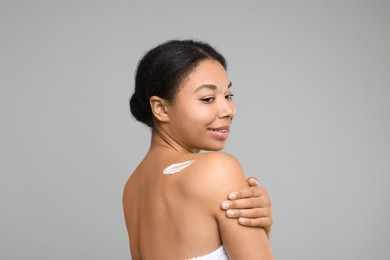 Photo of Young woman applying body cream onto back on grey background