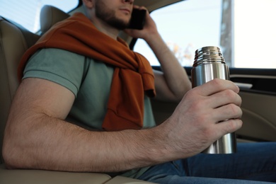 Man with thermos talking on phone in car, closeup