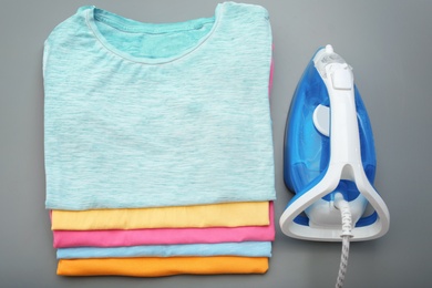 Photo of Folded clean clothes and iron on color background, top view