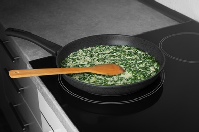 Photo of Tasty spinach dip with wooden spoon in frying pan on kitchen stove