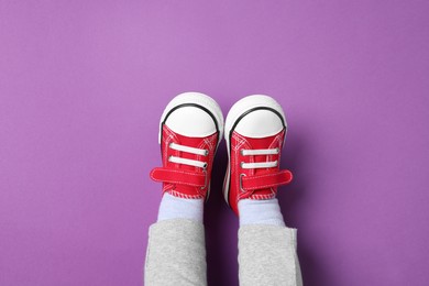 Little child in stylish red gumshoes on purple background, top view