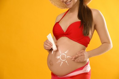 Photo of Young pregnant woman with sun protection cream on yellow background, closeup. Space for text