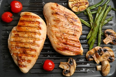 Tasty grilled chicken fillets and vegetables on frying pan, flat lay