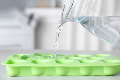 Photo of Pouring water into ice cube tray on table, closeup