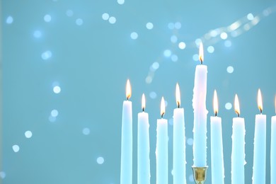 Photo of Hanukkah celebration. Burning candles on light blue background with blurred lights, closeup and space for text