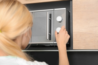 Photo of Young woman adjusting modern microwave oven in kitchen, closeup