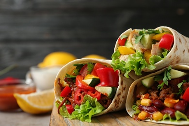 Photo of Board with delicious meat tortilla wraps on light table against black background, closeup