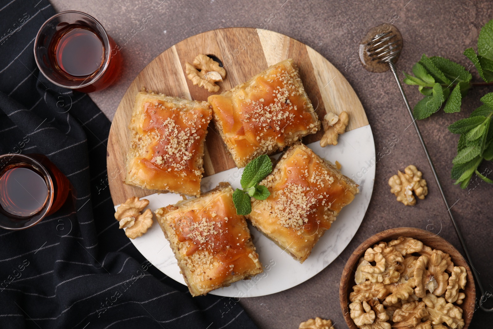 Photo of Eastern sweets. Pieces of tasty baklava, walnuts and tea on brown table, flat lay