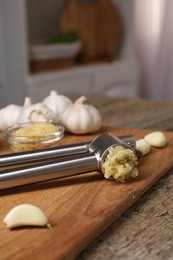 Photo of Garlic press, cloves and mince on wooden table in kitchen