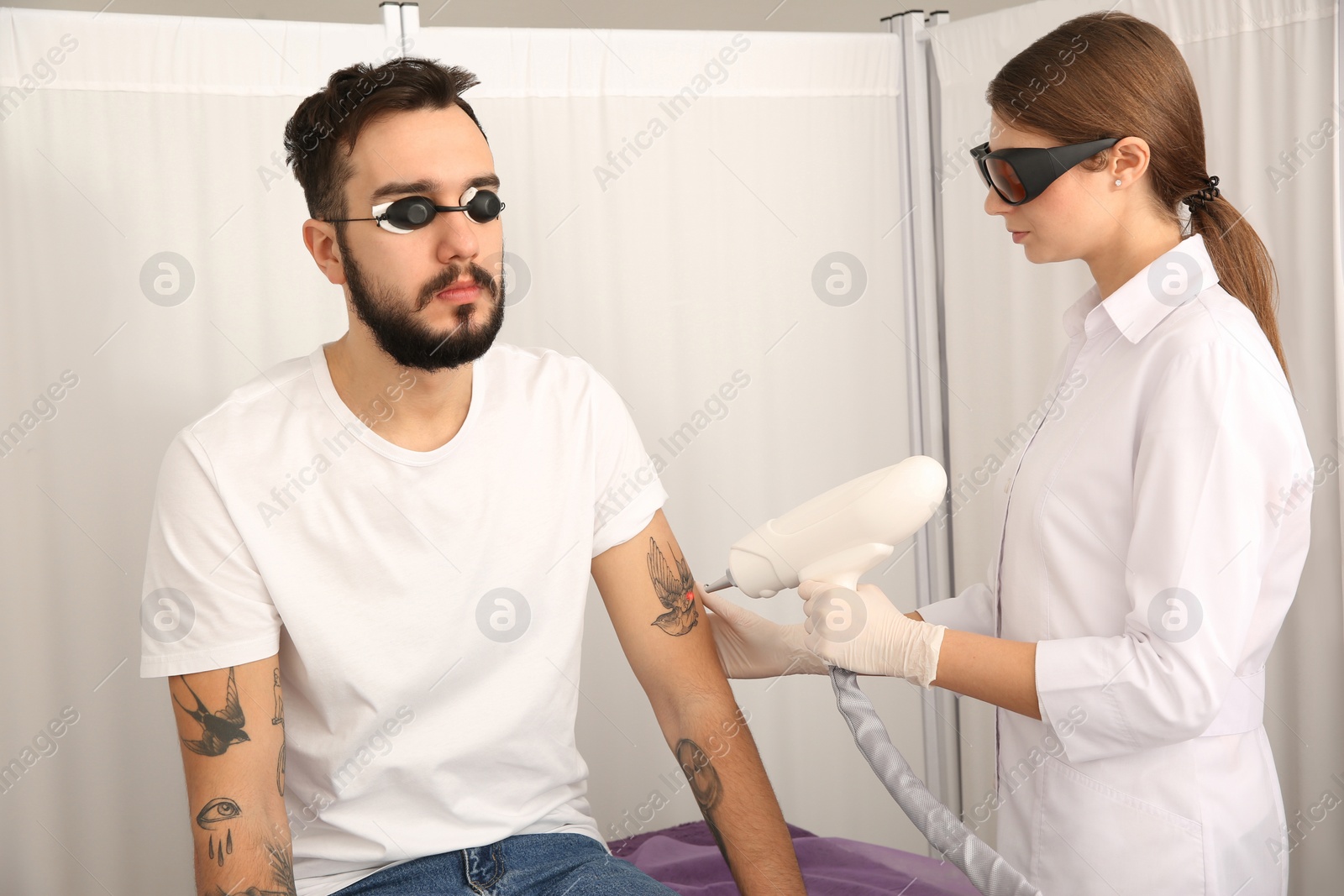 Photo of Young man undergoing laser tattoo removal procedure in salon