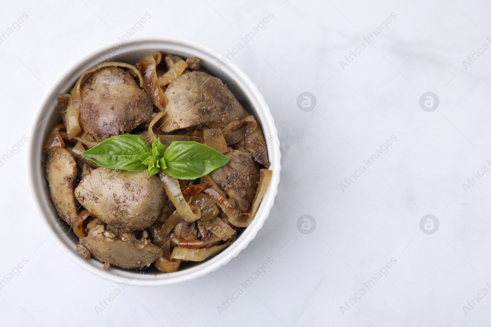 Photo of Delicious fried chicken liver with onion and basil in bowl on white marble table, top view. Space for text