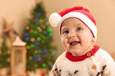 Cute little baby in Christmas sweater and Santa hat at home, space for text. Winter holiday