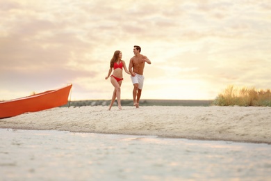 Photo of Happy young couple running together on sea beach at sunset