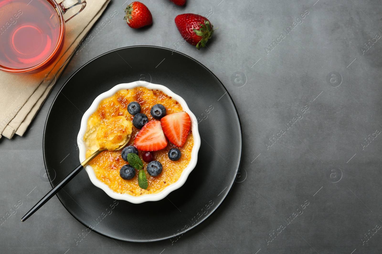 Photo of Delicious creme brulee with berries and mint in bowl served on grey table, flat lay. Space for text