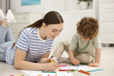 Photo of Mother and her little son drawing with colorful markers on floor at home