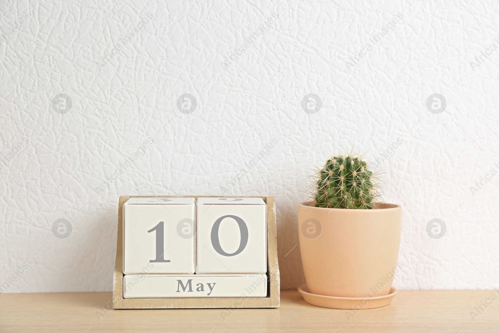 Photo of Wooden block calendar and cactus on table near white wall