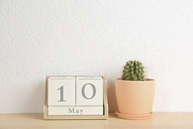 Wooden block calendar and cactus on table near white wall