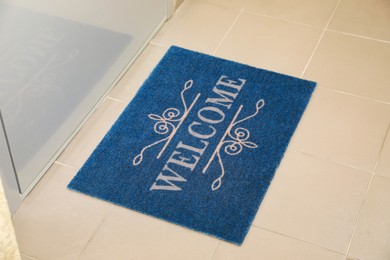 Photo of Beautiful blue doormat with word Welcome on floor near entrance