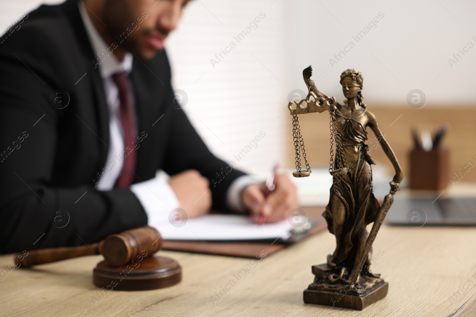 Photo of Lawyer working at table in office, focus on statue of Lady Justice