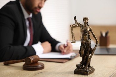 Photo of Lawyer working at table in office, focus on statue of Lady Justice