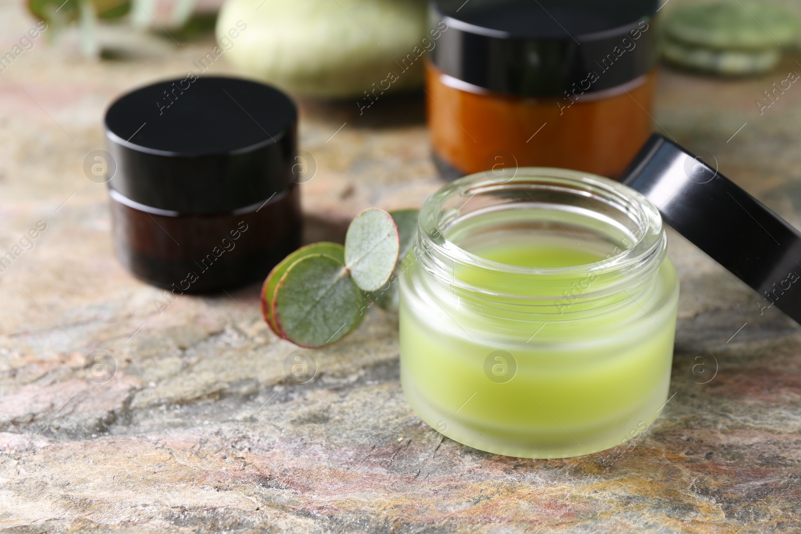 Photo of Jars of cream and eucalyptus leaves on textured table, closeup. Body care products