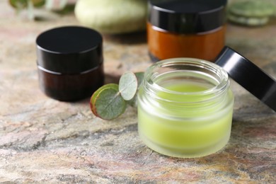 Jars of cream and eucalyptus leaves on textured table, closeup. Body care products