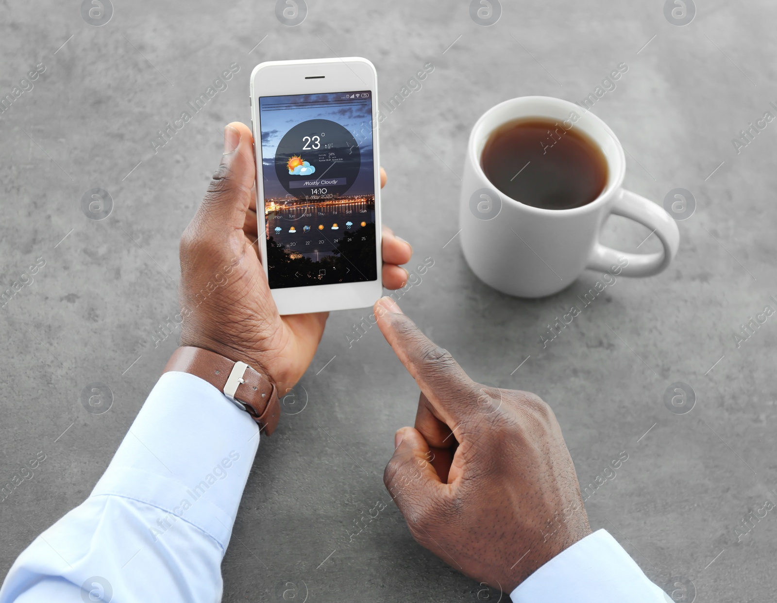 Image of African-American man using weather forecast app on smartphone at table, closeup