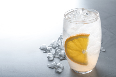 Photo of Water with ice cubes and orange on light grey table, closeup. Space for text