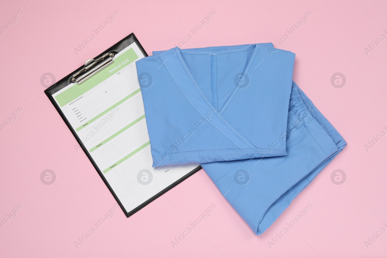 Photo of Medical uniform and clipboard on light pink background, flat lay