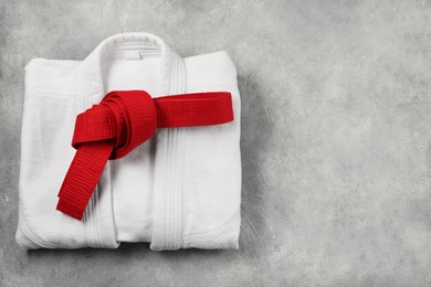 Red karate belt and white kimono on gray textured background, top view. Space for text